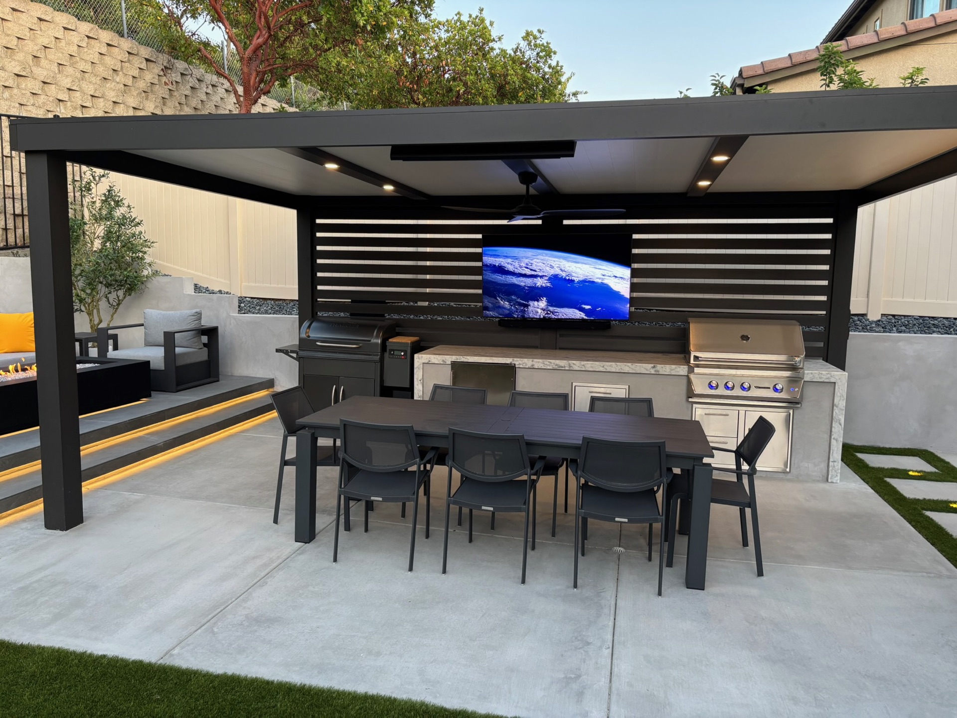 Louvered pergola, outdoor kitchen, and fire lounge at dusk, designed and built by Abshire Brothers Lawn & Landscape in Youngsville, Acadiana
