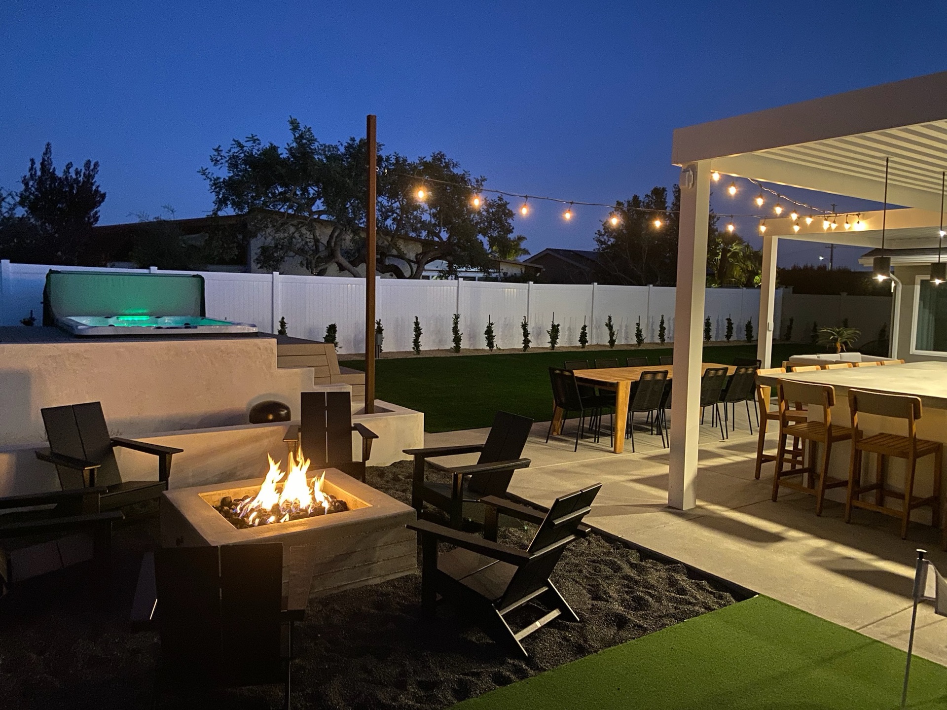 Resort patio with a fire pit, lit spa, and pergola at dusk, designed and built by Abshire Brothers Lawn & Landscape in Crowley, Acadiana