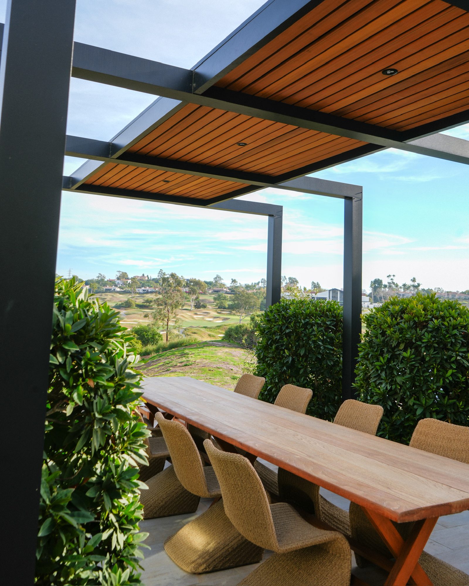 Teak dining table beneath the black steel arches with the golf course behind