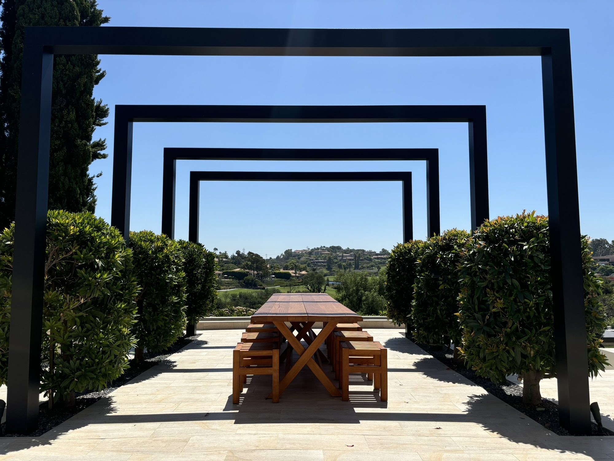 Four black steel arches framing a teak dining table with views over The Farms golf course in Kaplan