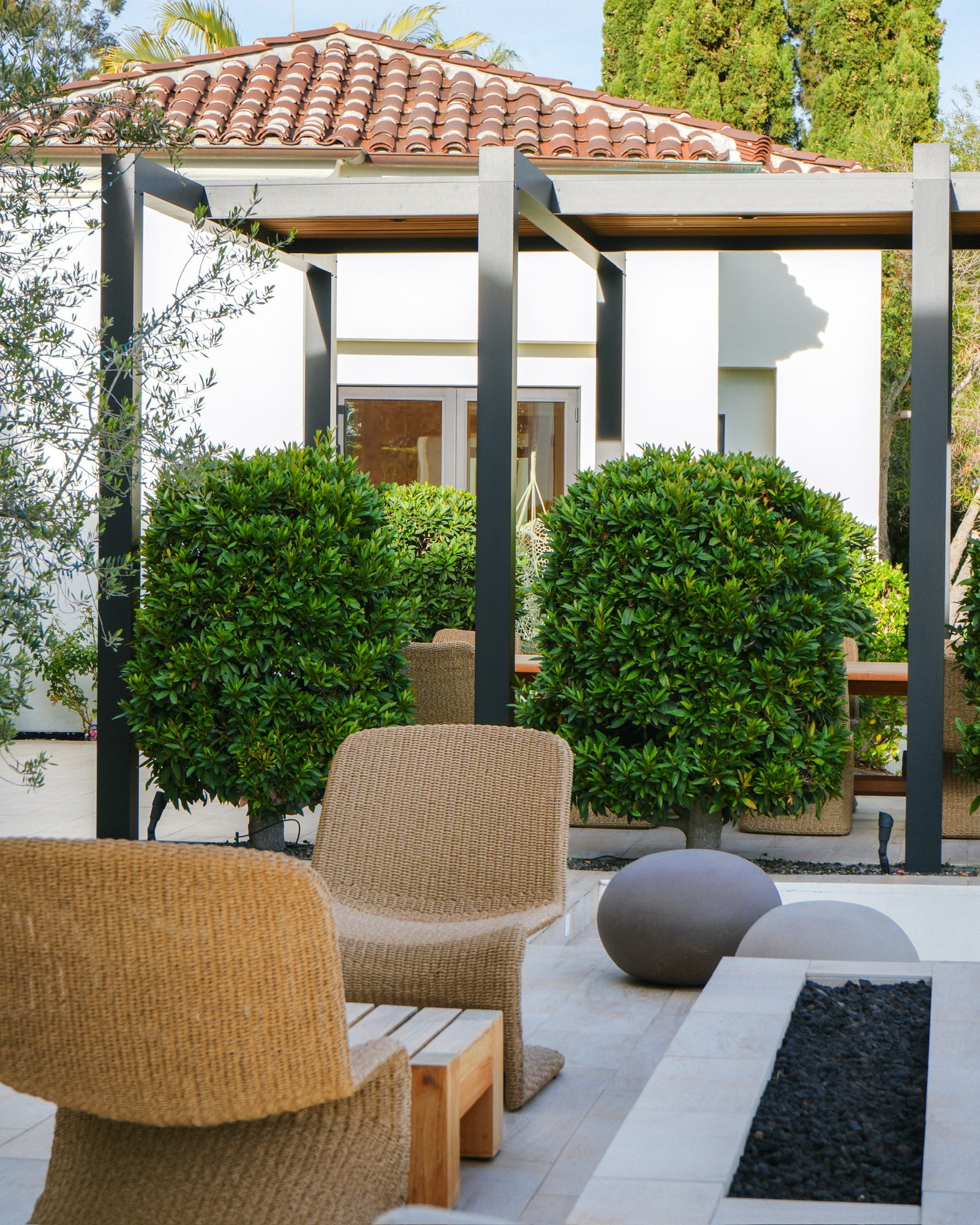 Woven lounge chairs on the covered patio beside clipped topiary