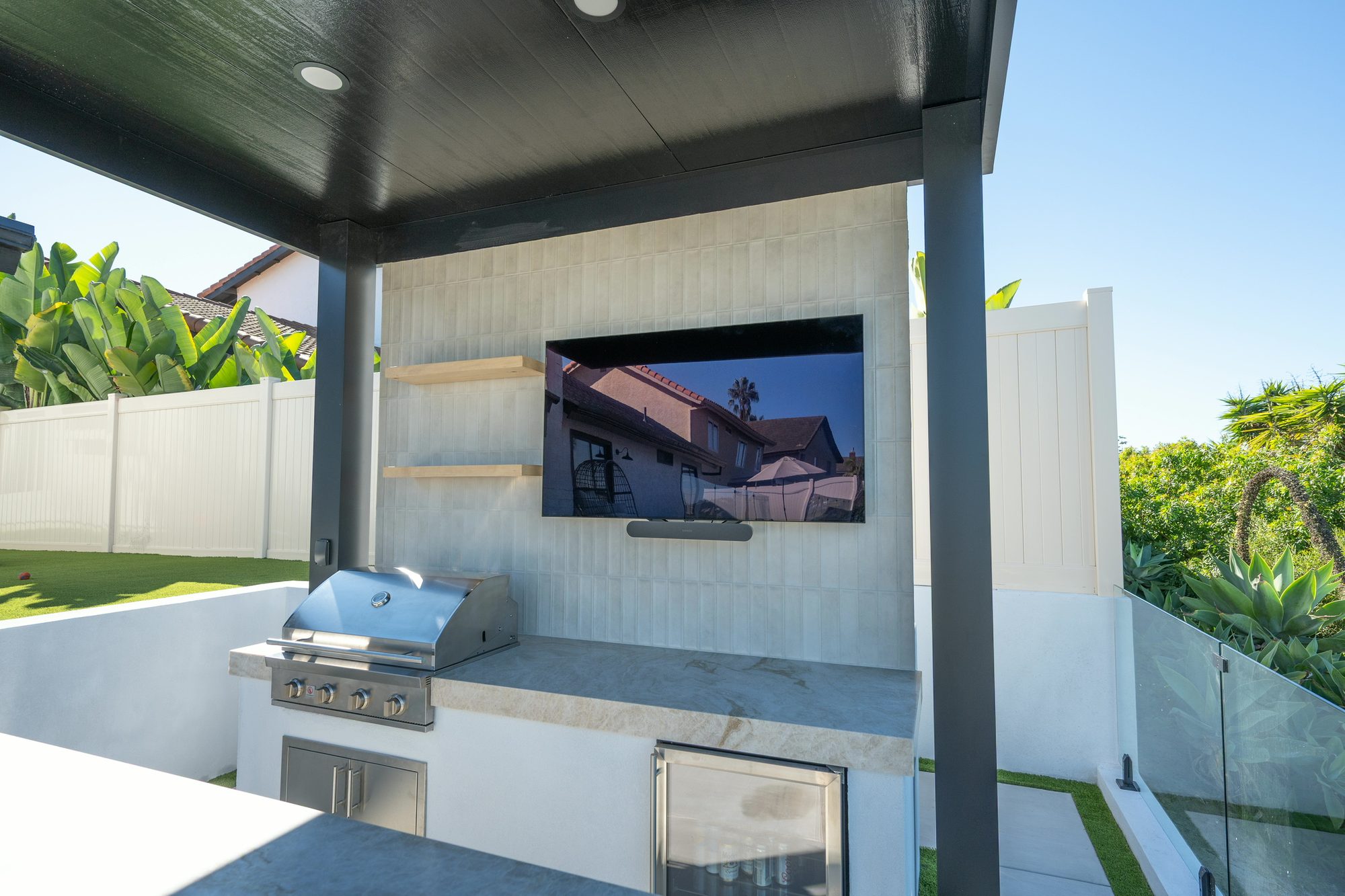 Outdoor kitchen with a built-in grill, integrated television on a tile feature wall, and a floating Taj Mahal quartzite bar in Lafayette