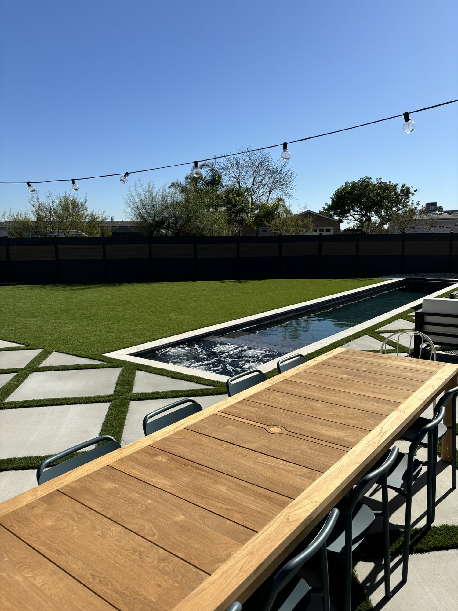Teak bar-height dining table beside the pool with string lights
