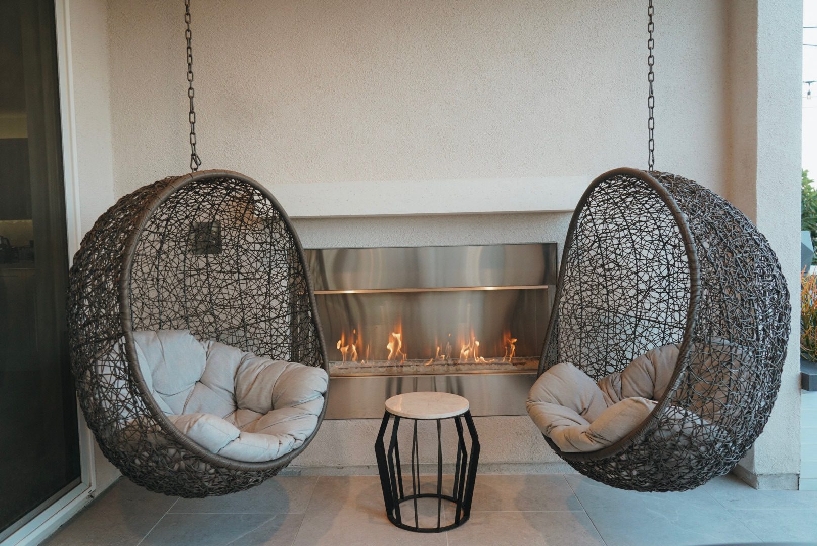 Hanging egg chairs beside a fireplace under the Kuzma pergola