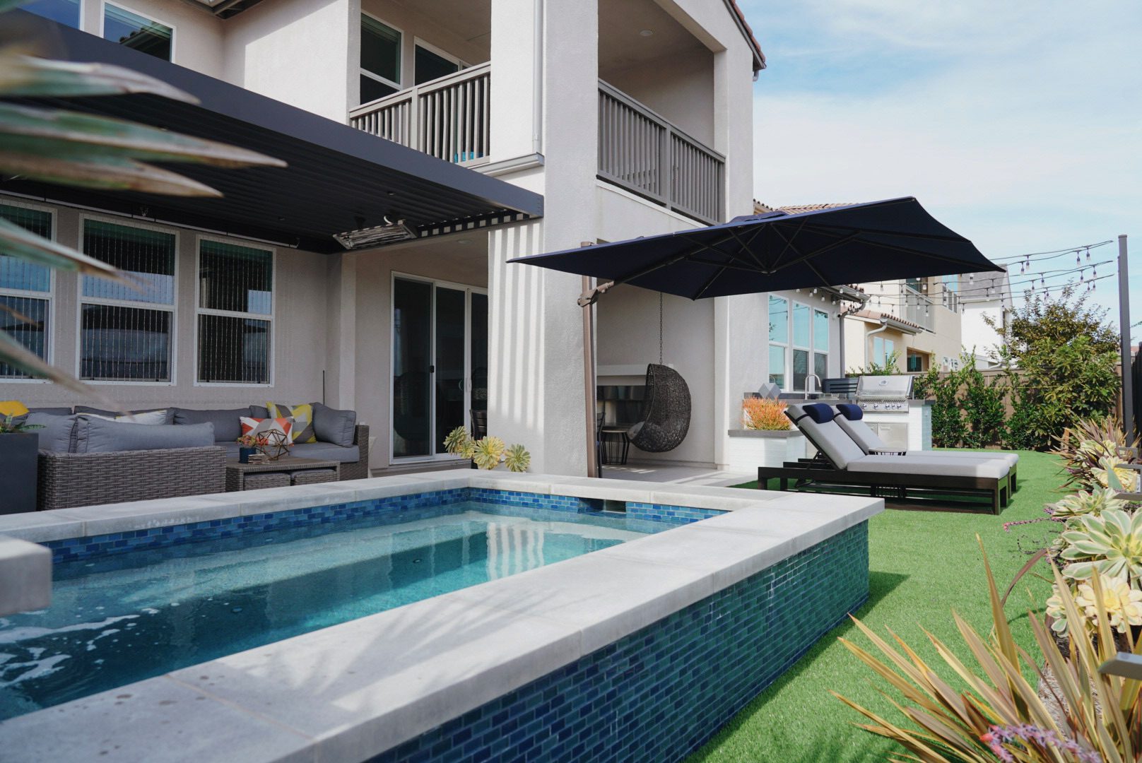 Kuzma backyard in Crowley with a blue glass-tile spool, cantilever pergola and outdoor kitchen