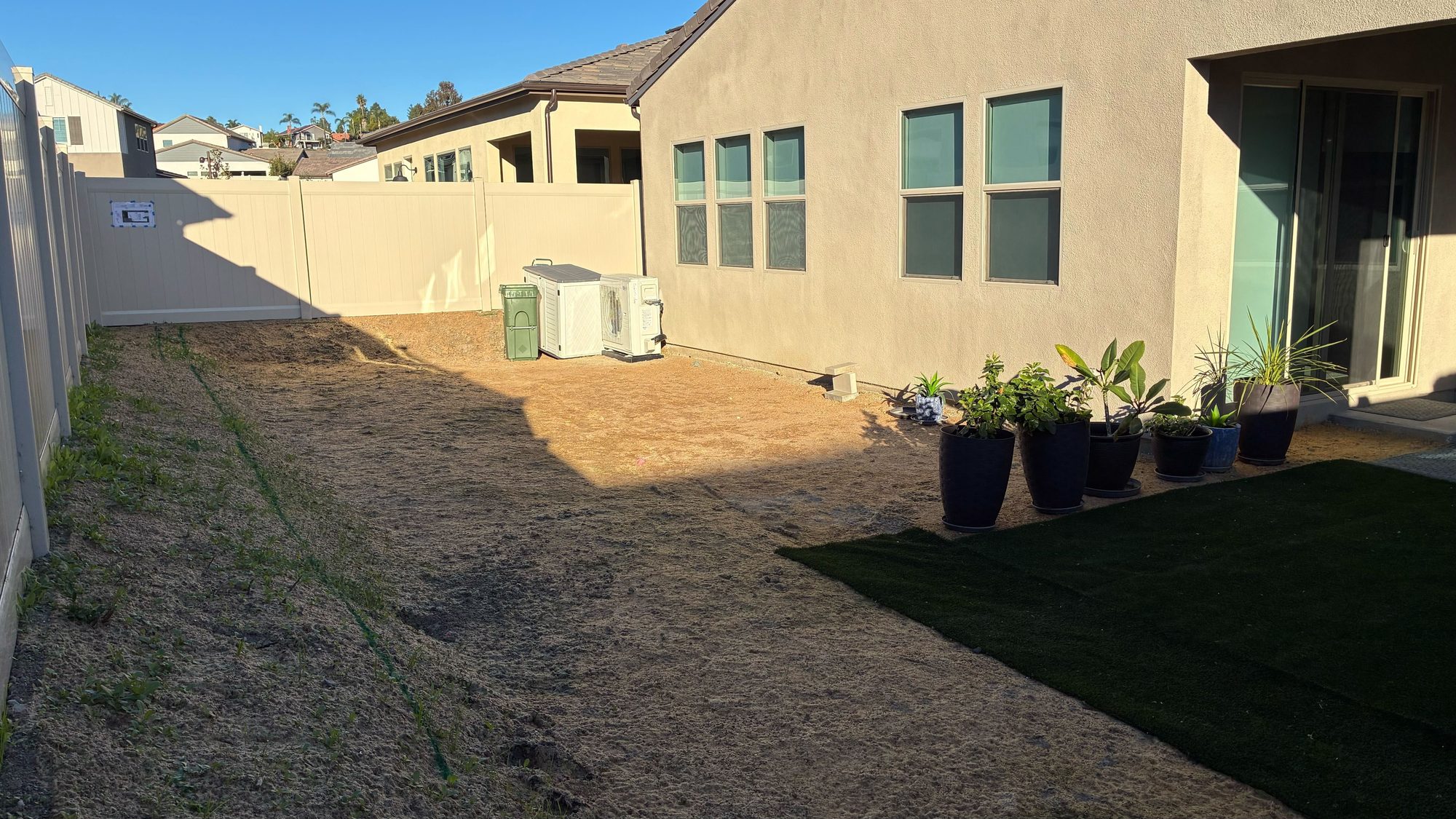 Before: the bare dirt Riley backyard with exposed AC units against a vinyl fence