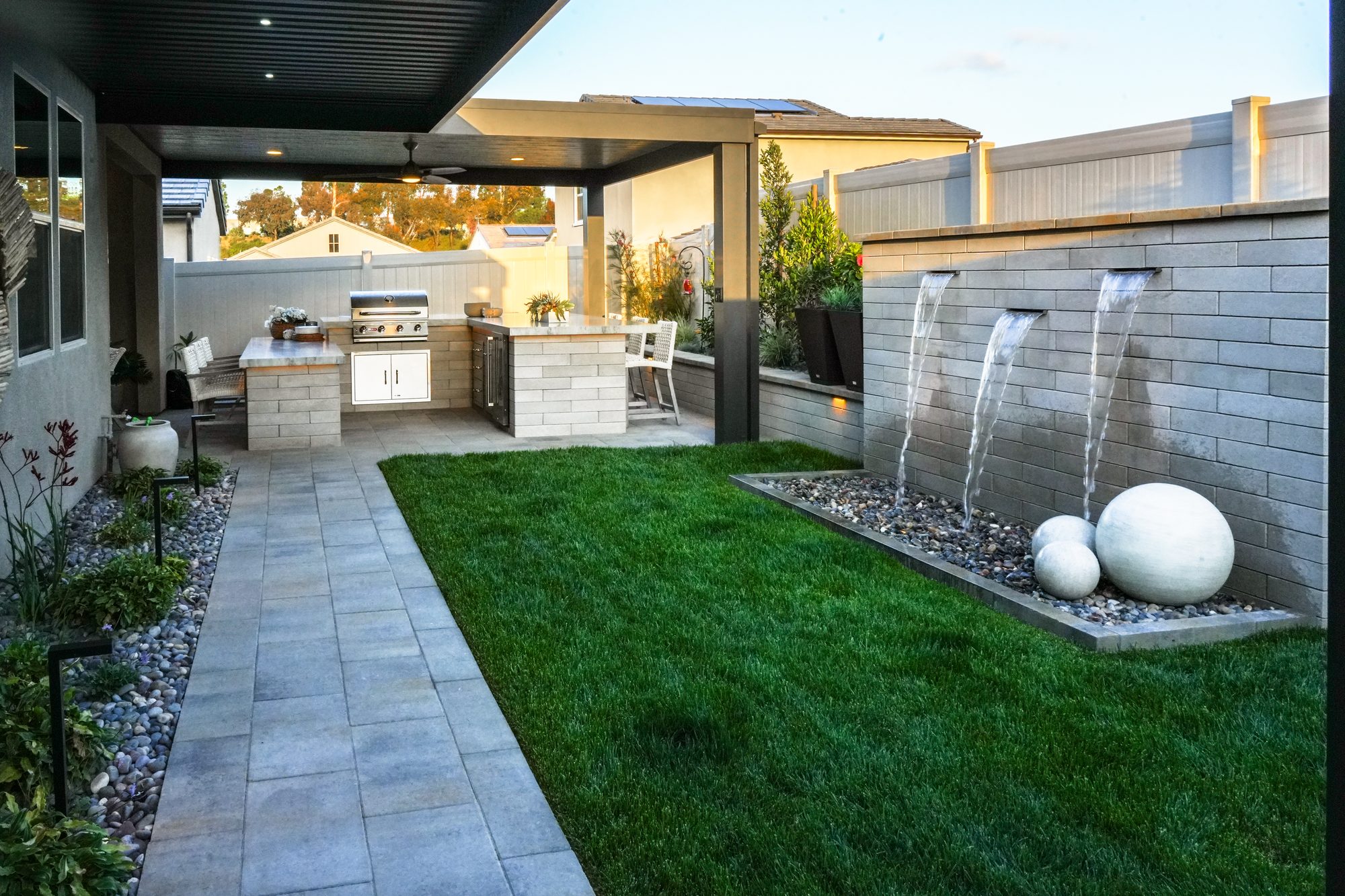 Riley backyard in Church Point with a covered outdoor kitchen, sod lawn and a Melville-block water feature with spheres