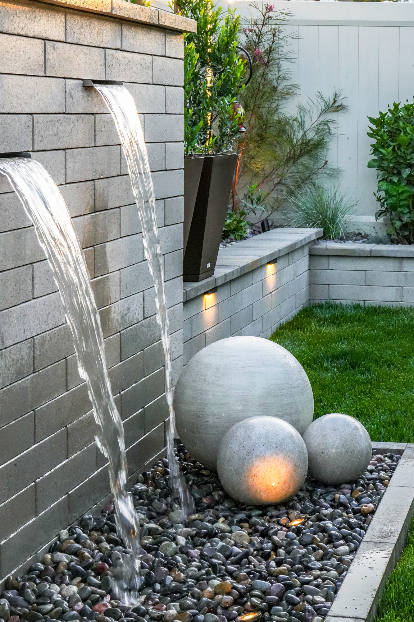 Melville-block water feature with two scuppers cascading past stone spheres into a dry-riverbed reservoir