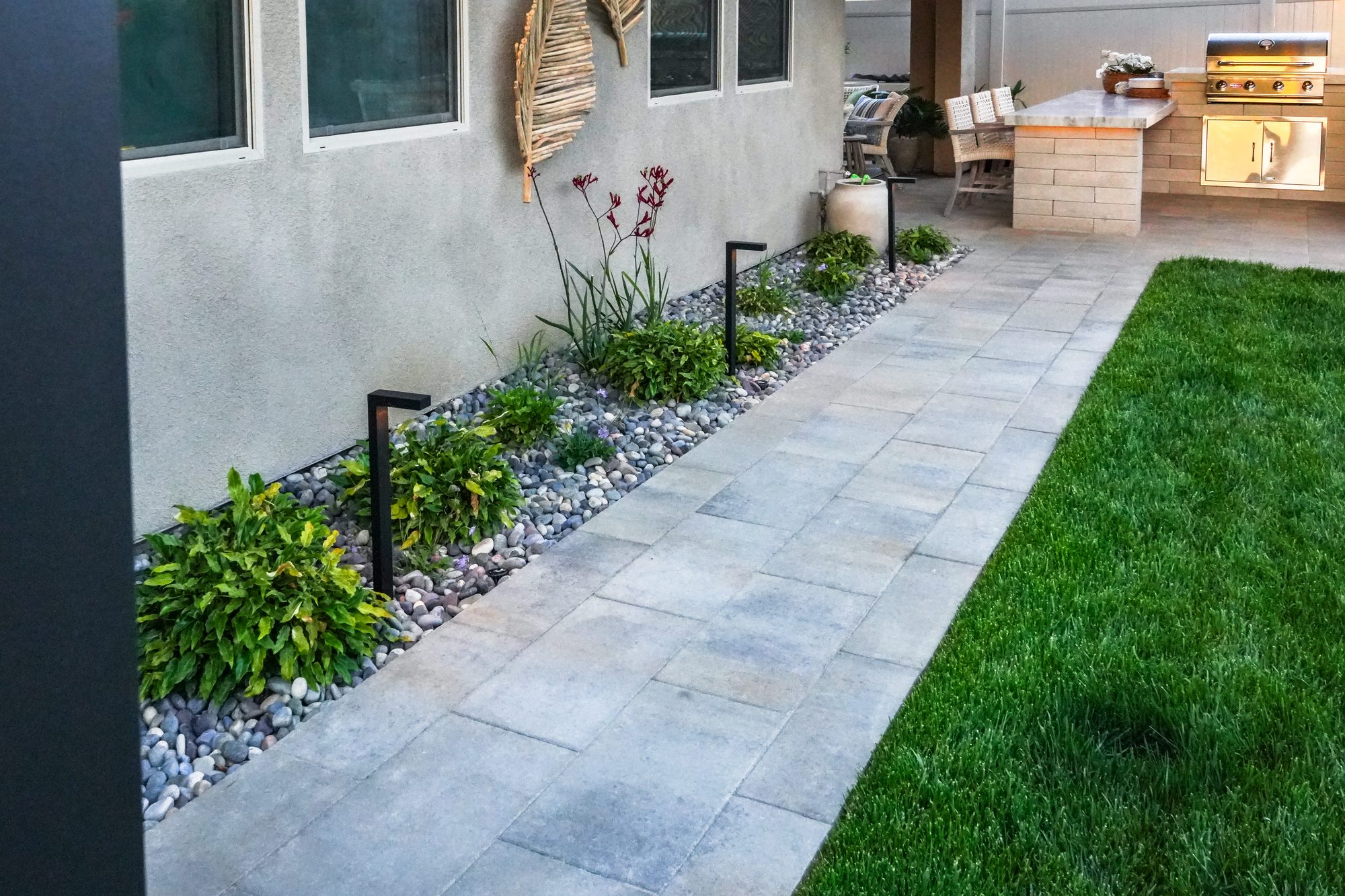 Paver walkway past the water feature and sod lawn toward the kitchen